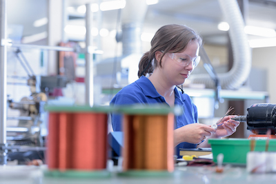 Female worker assembling electromagnetic coils in electronics factory